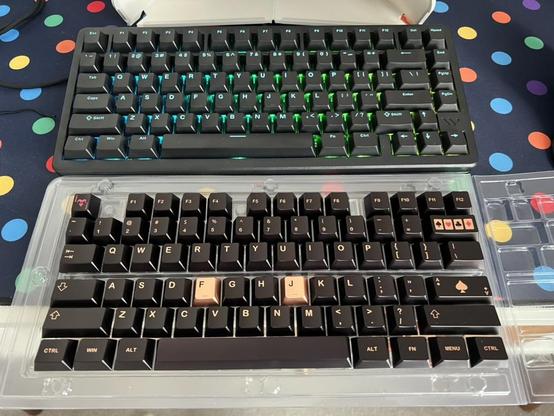 A mechanical keyboard, lit up, with an open tray of keycaps sat in front of it.