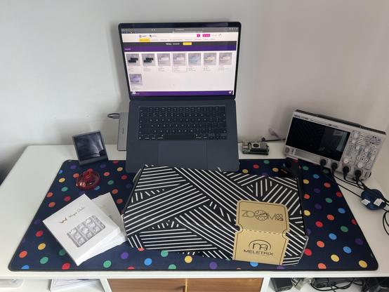 A boxed Zoom65 V3 keyboard kit and switches sat on a dotty deskmat in front of a MacBook.