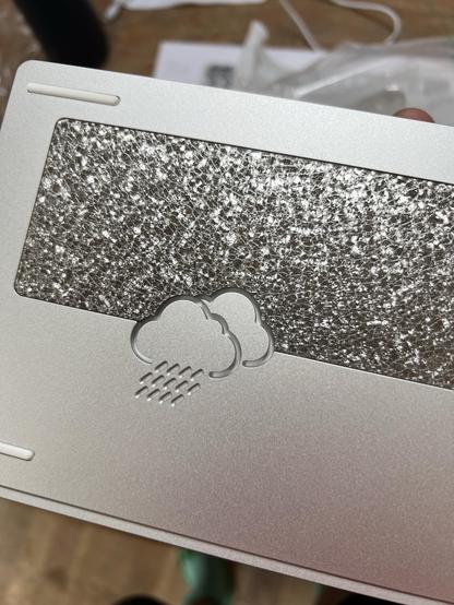 A shiny, textured metal badge set within the back of a mechanical keyboard.