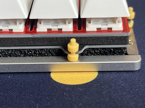 A vibrant yellow dumbbell shaped grommet isolating a keyboard PCB from its aluminium bottom case.