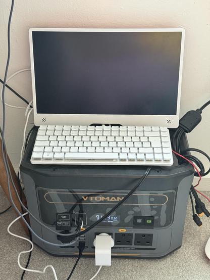 A Pi 500+ single board computer/mech keyboard combo and a Pi monitor sat on top of a chunky portable battery. Wires trail roughly everywhere.