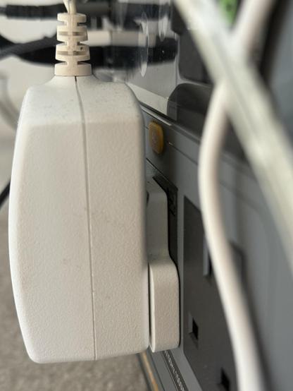 A closeup of a plug socket on a portable battery. A plug with a large wall wart is plugged in and totally blocking a small yellow on/off button.