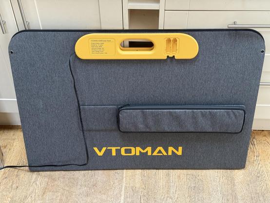 A huge folded stack of solar panels with a bright yellow carry handle, a nice fabric outside and a carry pouch for the adapter cable.