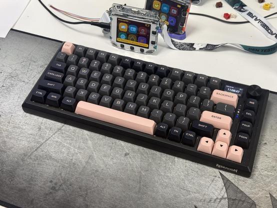 A black aluminium 75% mechanical keyboard with black, grey and salmon pink keycaps.