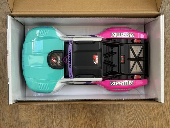 A remote control car styled like a desert racing truck and coloured very striking shades of teal, white and pink.