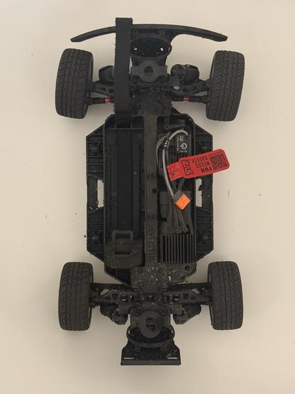 A dirty muddy RC car with its top shell and battery removed, sat in the bottom of a bathtub.