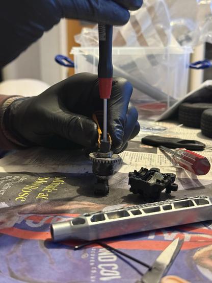 Hands clad in black nitrile gloves disassembling an RC differentiate on newspaper.