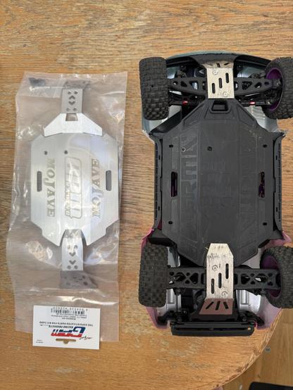 A plastic package with a full underbody metal skid plate, sat alongside an upturned RC car with small separate front and back skid plates installed.