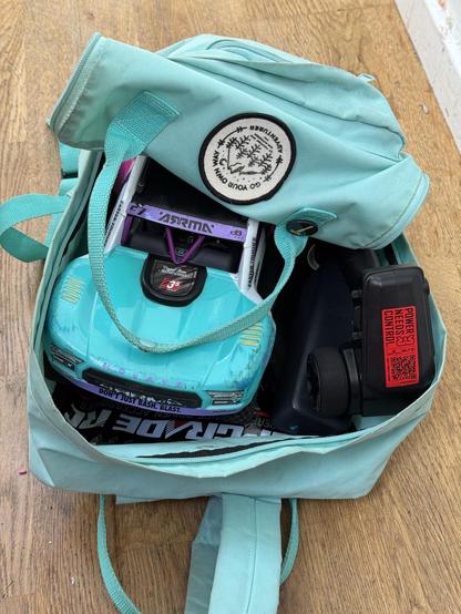 A scuffed and scraped RC car tucked into a teal backpack with its remote, a portable battery and some other spare bits and bobs.