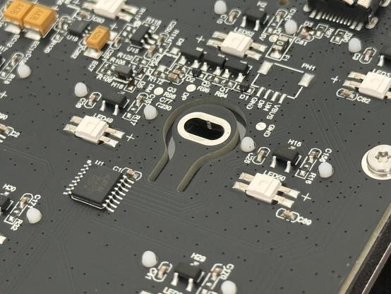 A PCB with a small antennae-like circle on a stem shape routed out of it, forming slightly flexible cantilever isolation for one of the screws securing it to the base.