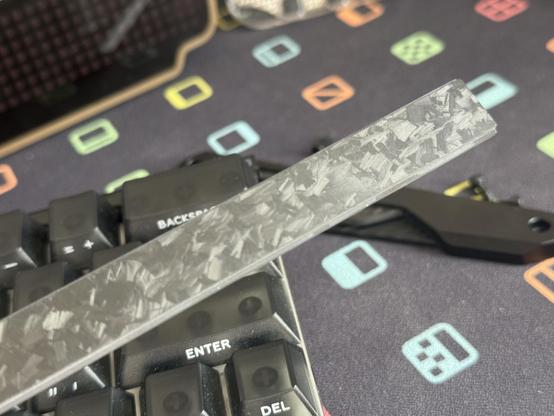 The carbon fibre badge from the front edge of the keyboard, it’s a long strip with a sort of random pattern of carbon fibre fragments in it.