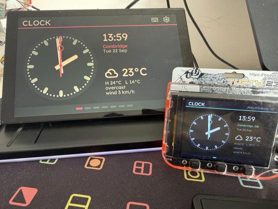 An 8” touchscreen display sat on a deskmat with a smaller Badgeware Tufty display sat in front and to the side. Both display the same clock and weather info.